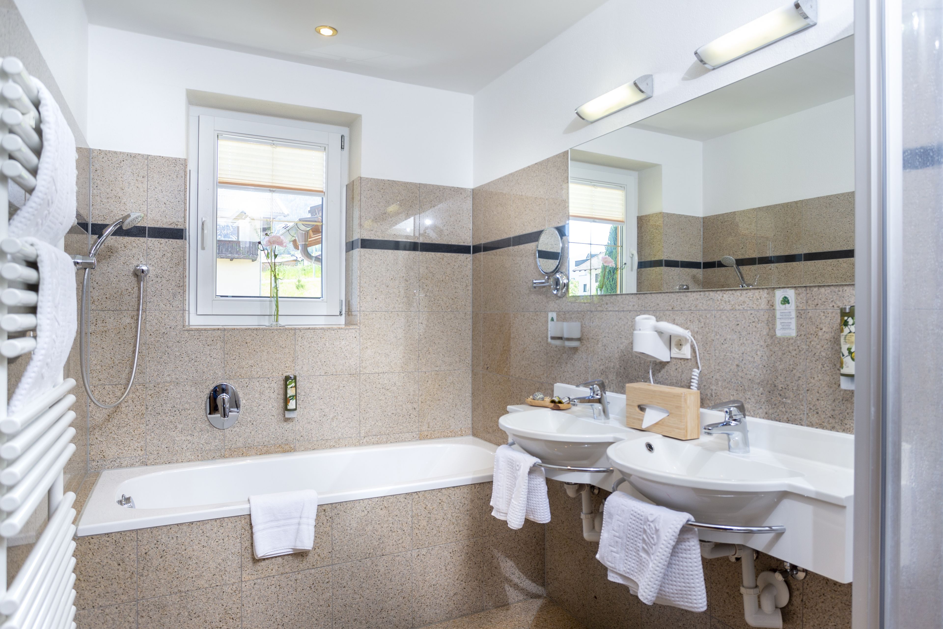 A modern bathroom with a bathtub, two sinks, and a large mirror.