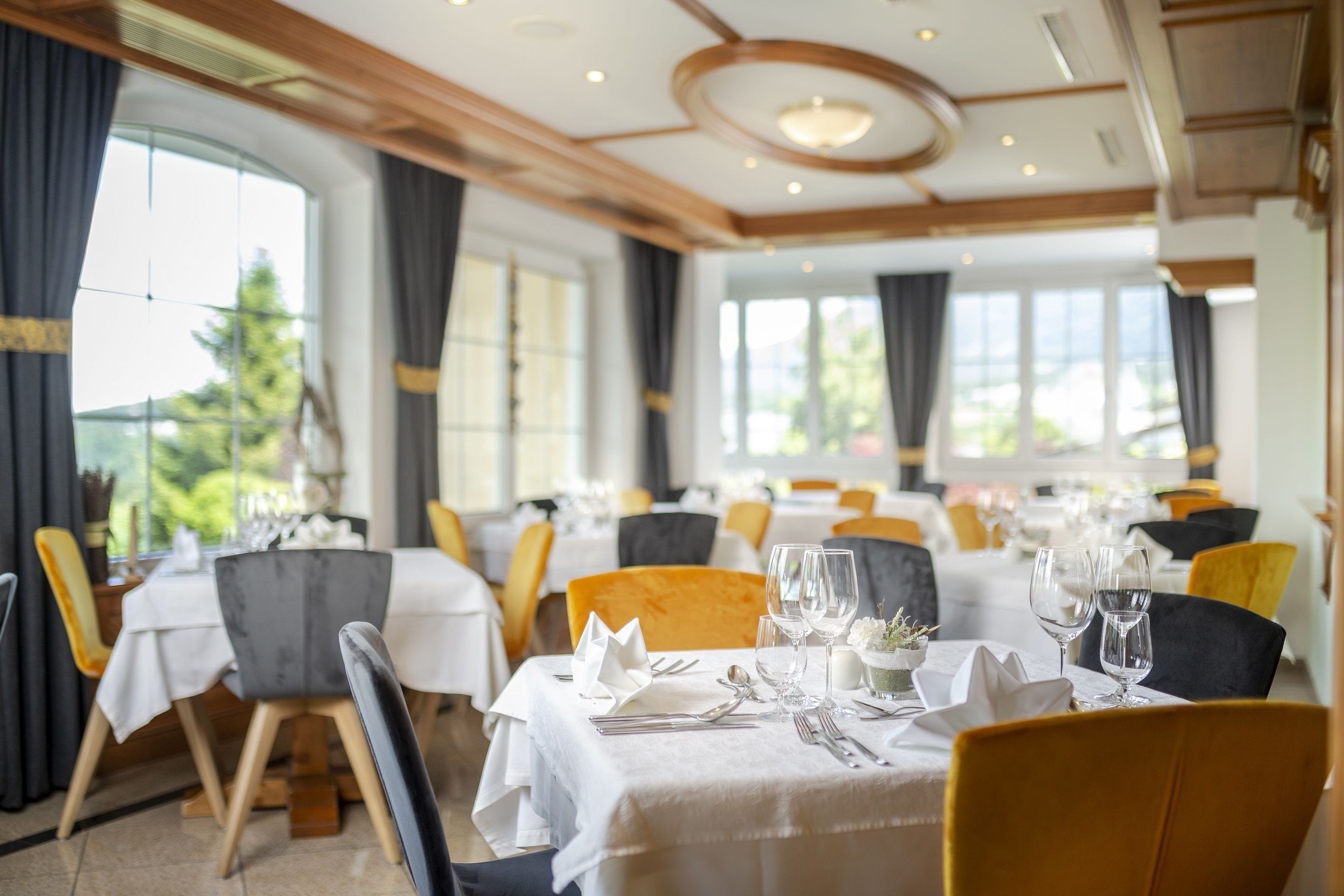 A restaurant with round tables, white tablecloths, and yellow chairs.