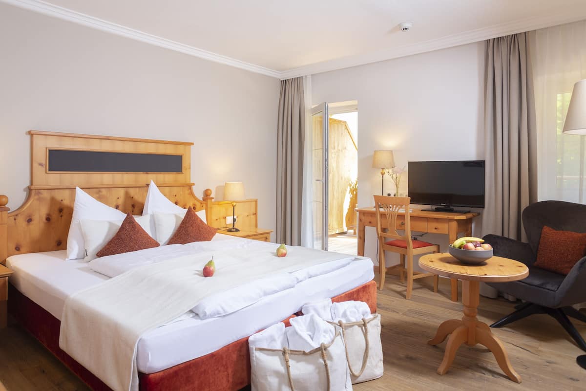 A hotel room with a large bed, a desk with a computer, a TV, and a seating area with a chair and a small table.