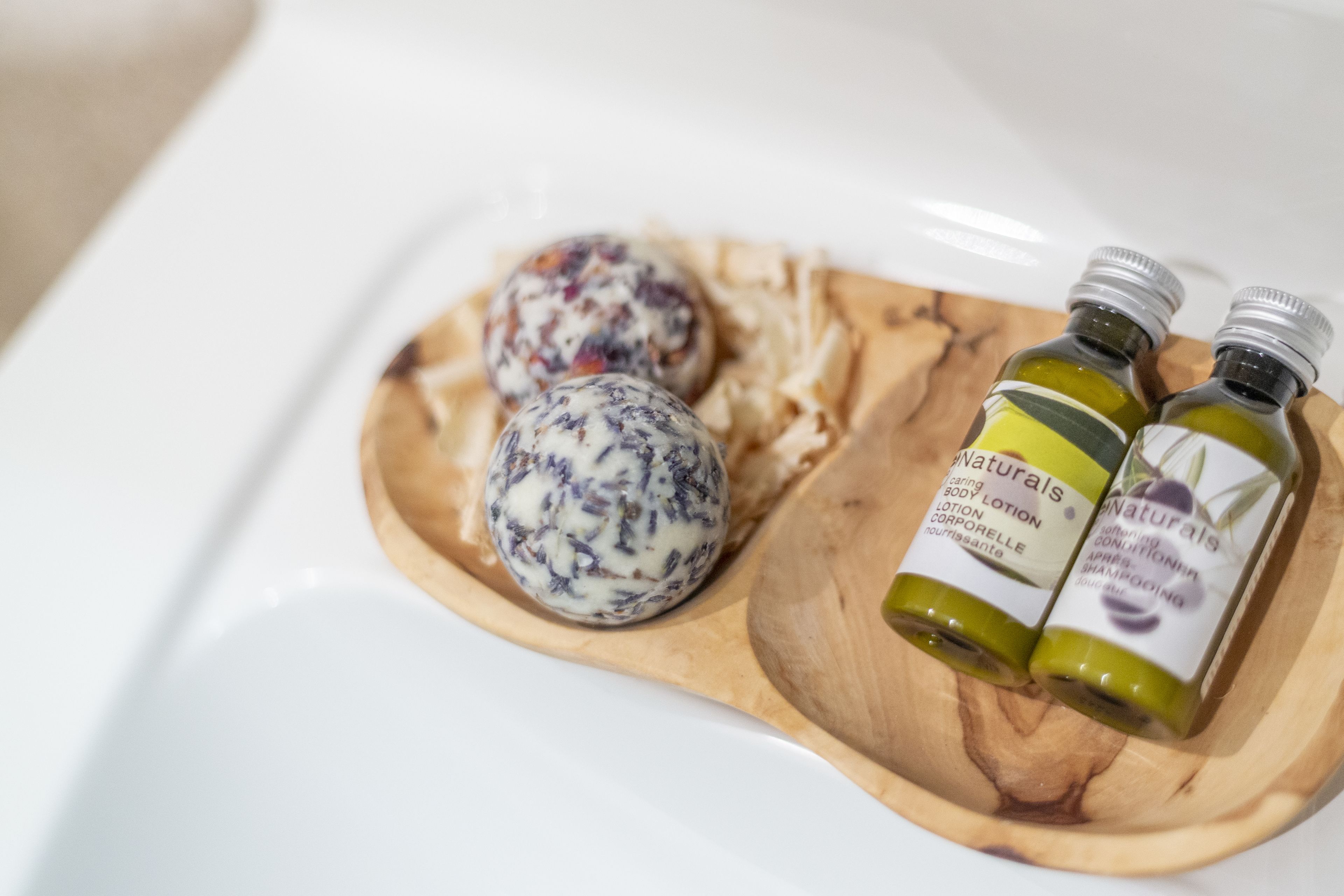 A wooden tray with two bottles of Naturals body lotion and two spherical objects on a white surface.