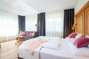 Una habitación de hotel con una cama grande, un sofá, una mesita pequeña y un armario de madera.