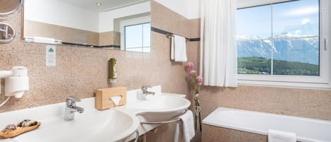 A modern bathroom with two sinks, a bathtub, a large mirror, and a window with a mountain view.