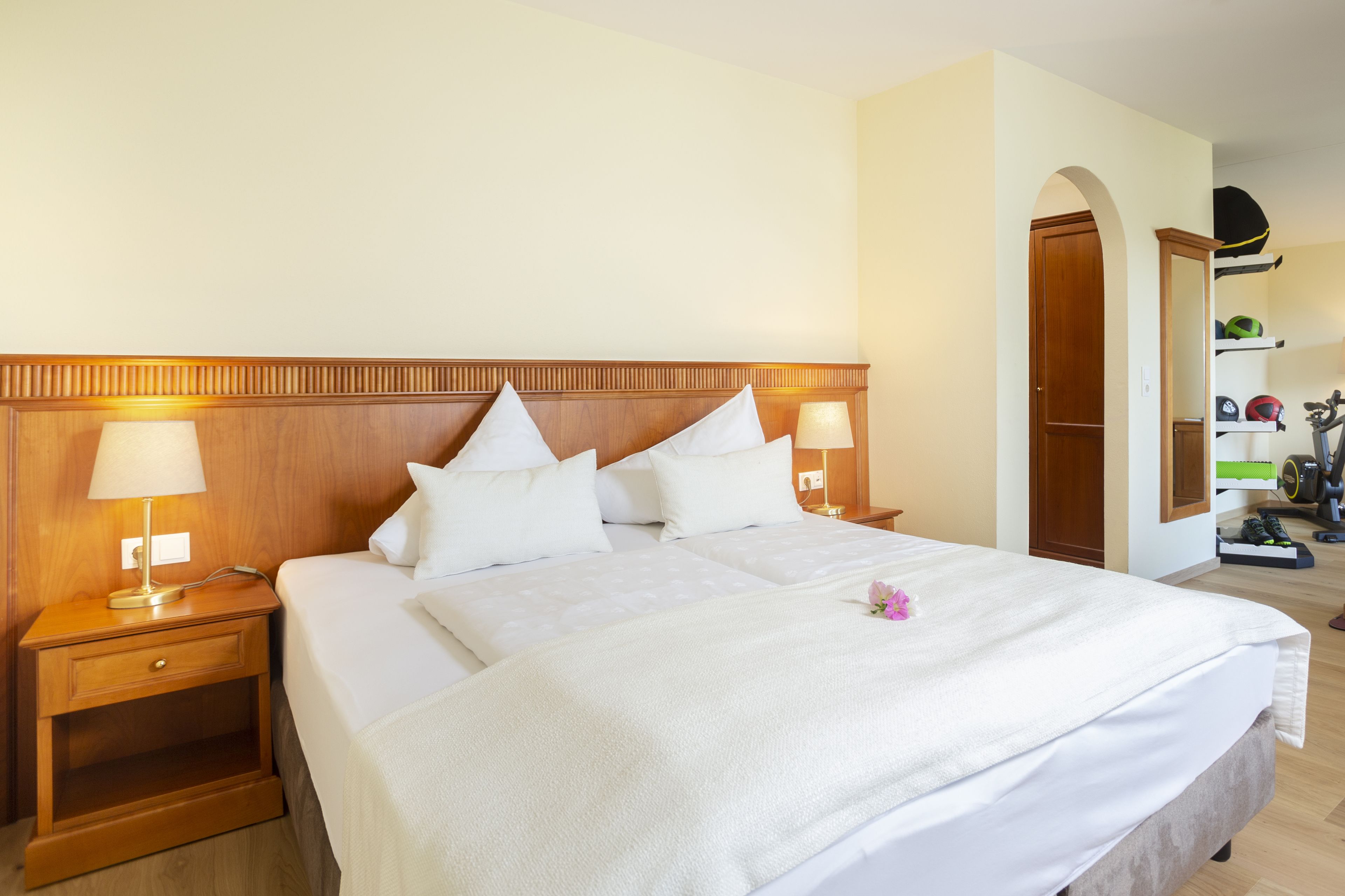 A neatly made bed with white linens and pillows, a wooden nightstand with a lamp, and a mirror on the wall.