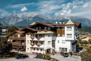 Un hotel de varios pisos con balcones, un estacionamiento y montañas al fondo.