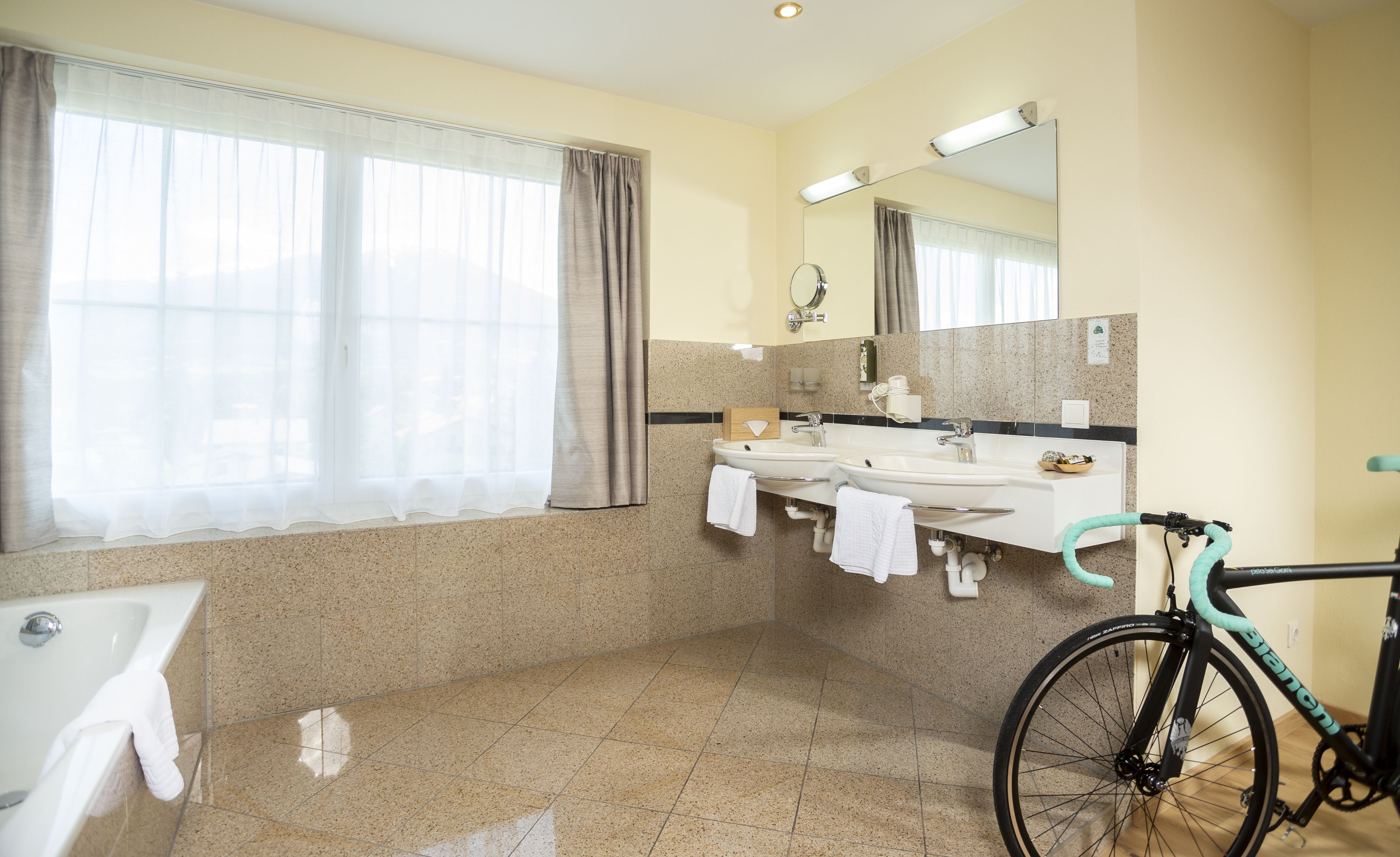 Een badkamer met een bad, twee wastafels, een spiegel en een fiets.