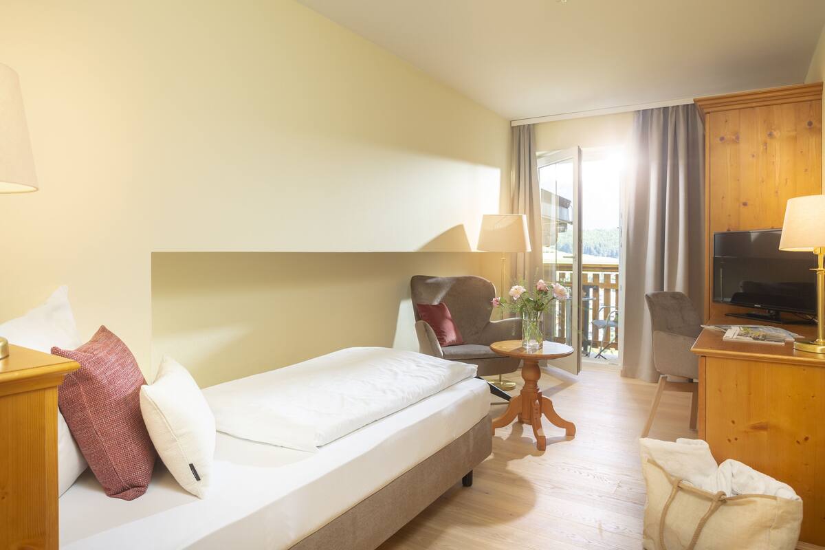 A hotel room with a bed, a chair, a small table, a TV, and a balcony with a view.