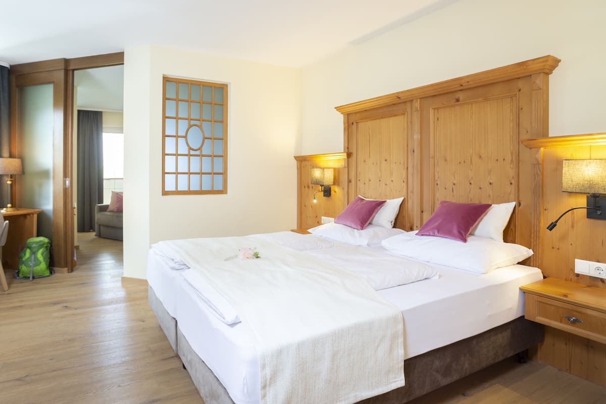 A hotel room with a large bed, wooden headboard, two bedside lamps, and a small desk with a lamp.