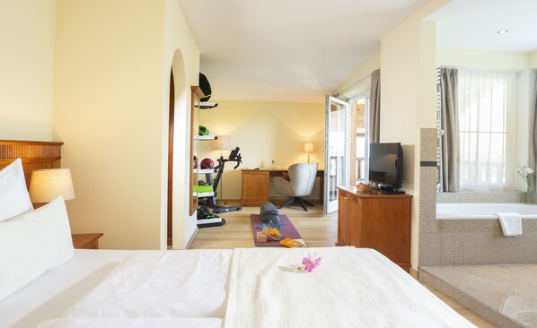 Habitación de hotel con cama, escritorio, silla, televisor y baño con bañera.