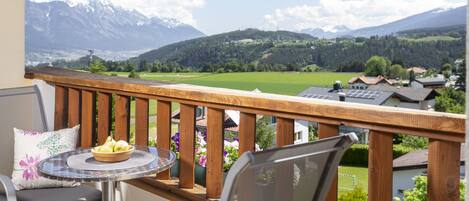 Un balcón con mesa y sillas, con vistas a un paisaje montañoso con casas y vegetación.