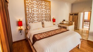 Una cama bien hecha con un cabecero decorativo, lámparas de noche y una mesita de madera con un objeto rojo encima.