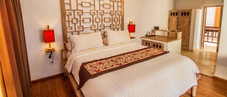 Una cama bien hecha con un cabecero decorativo, lámparas de noche y una mesita de madera con un objeto rojo encima.