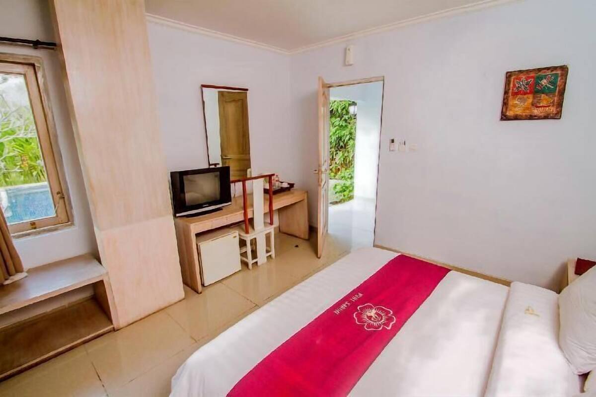 A bedroom with a bed, a desk, a television, and a door leading to a balcony.