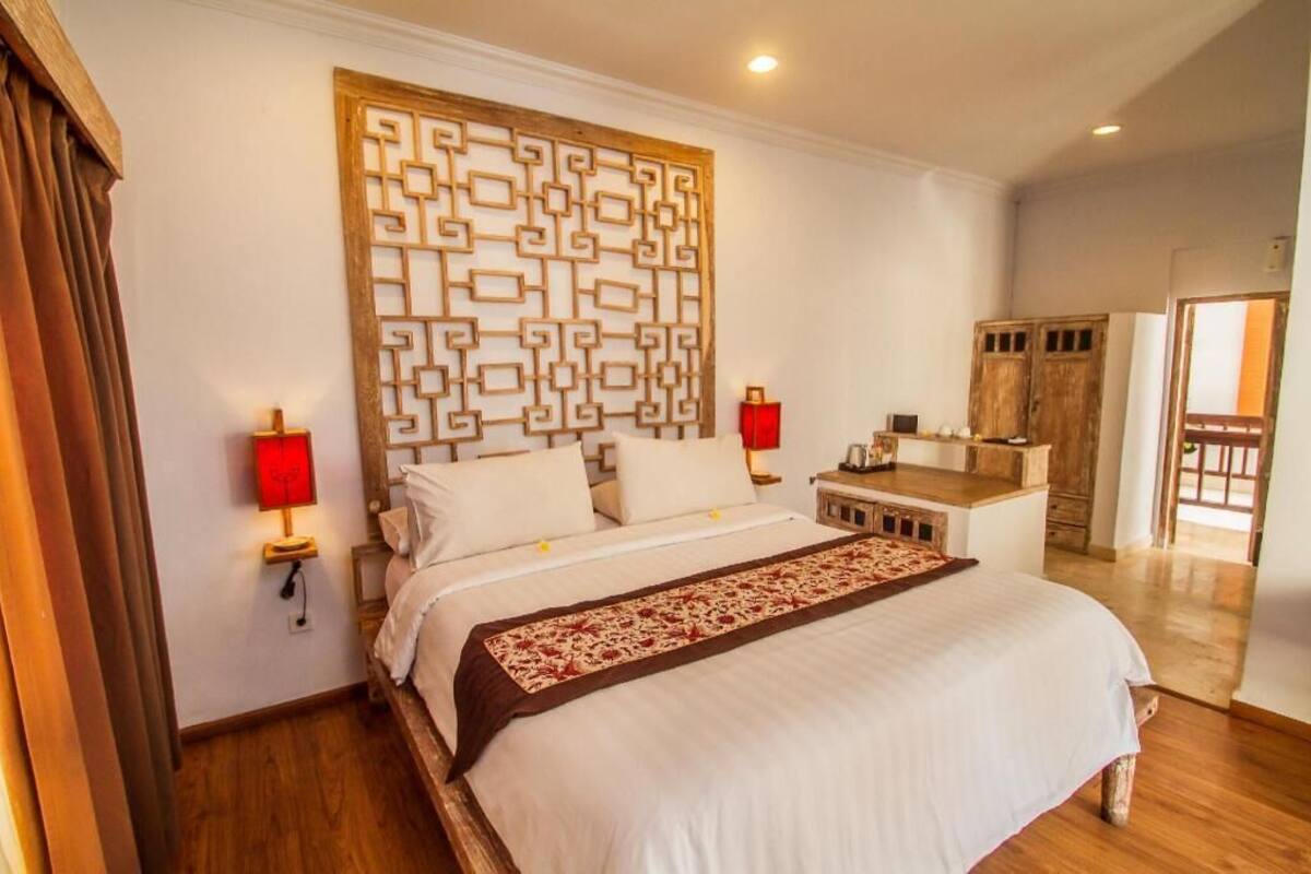 A bedroom with a large bed, a decorative wall panel, bedside lamps, and a wooden nightstand.