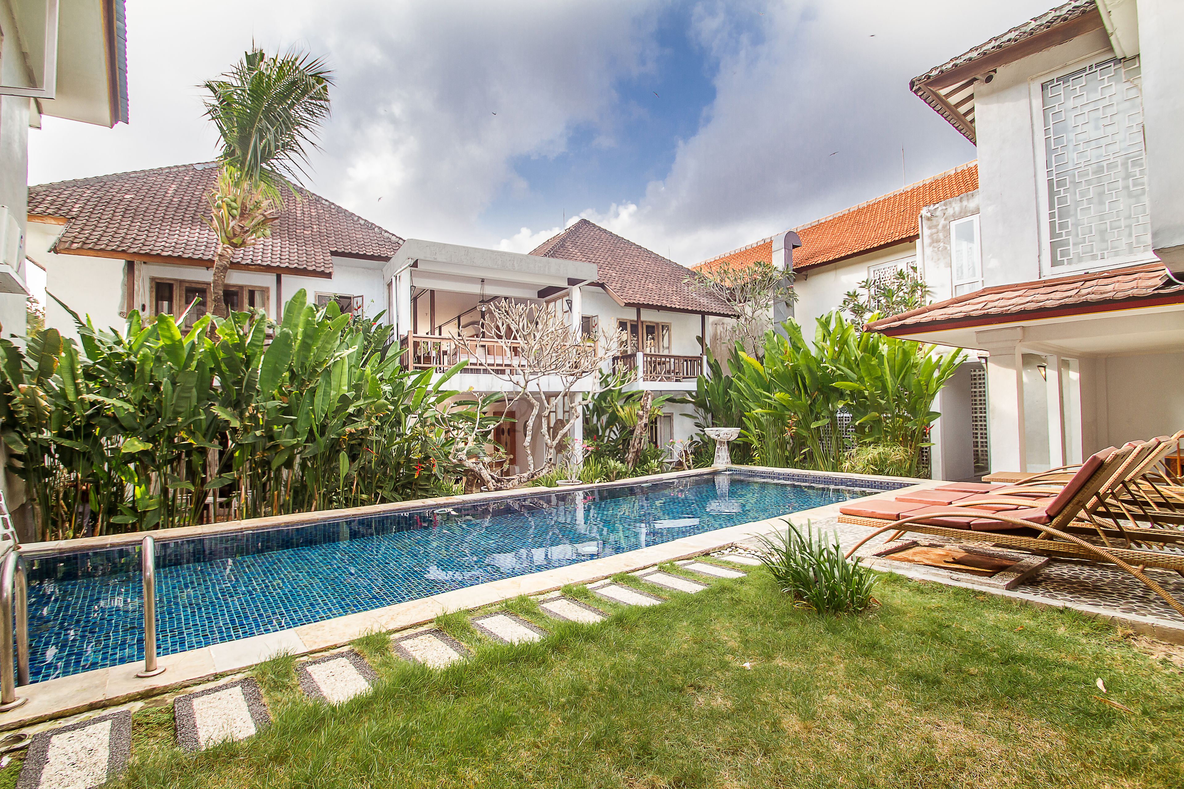 A swimming pool with a tiled deck, surrounded by lush greenery and a clear sky.