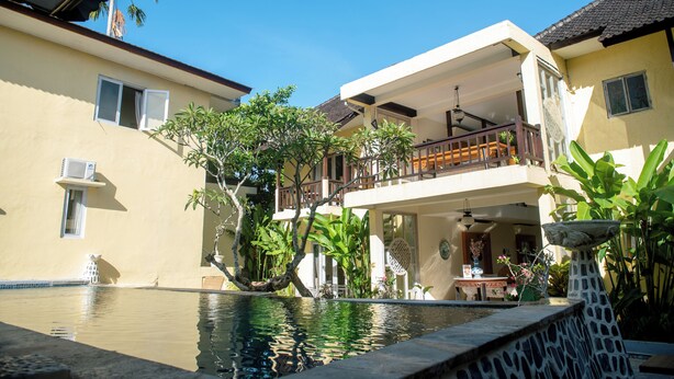 Una casa de dos pisos con balcón, piscina y abundante vegetación.