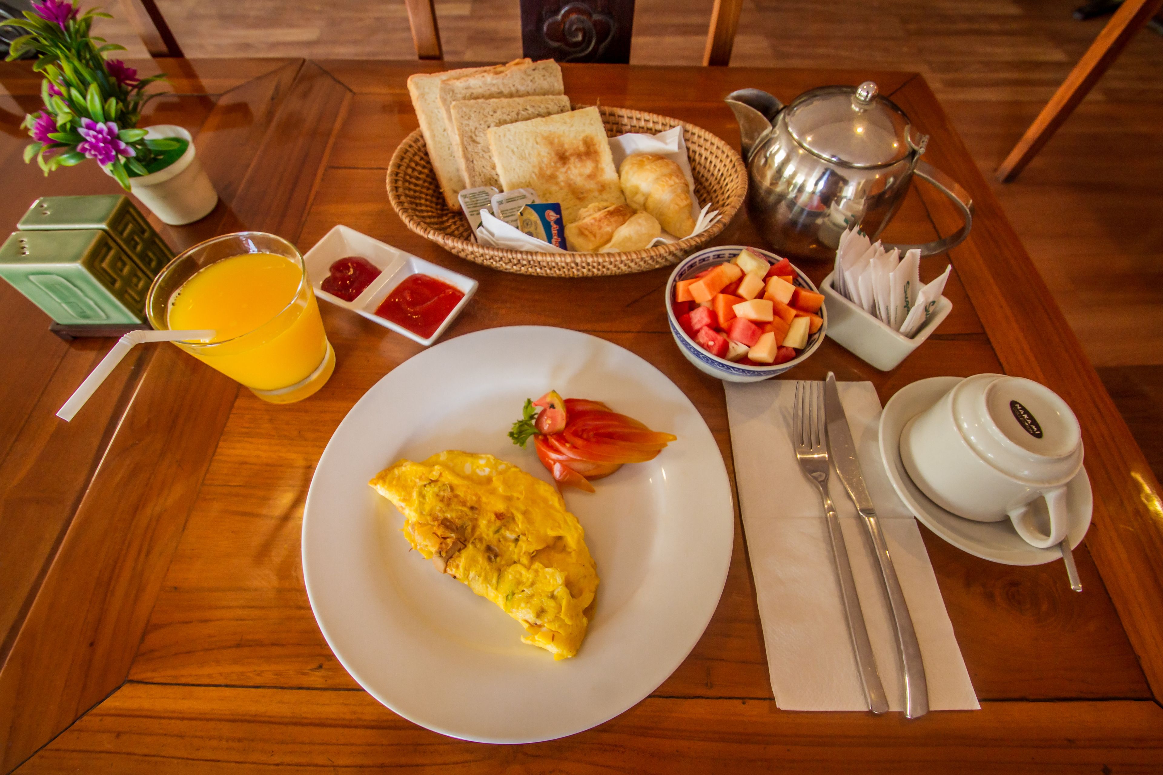 Een ontbijtsetting met toast, eieren, fruit en een theepot op een houten tafel.