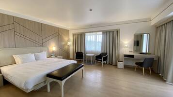 Una habitación de hotel con una cama grande, un escritorio, dos sillas, una mesita y un espejo.