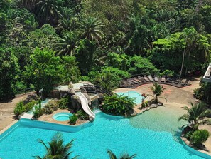 Un resort con una gran piscina, una cascada y un área de descanso rodeada de exuberante vegetación.