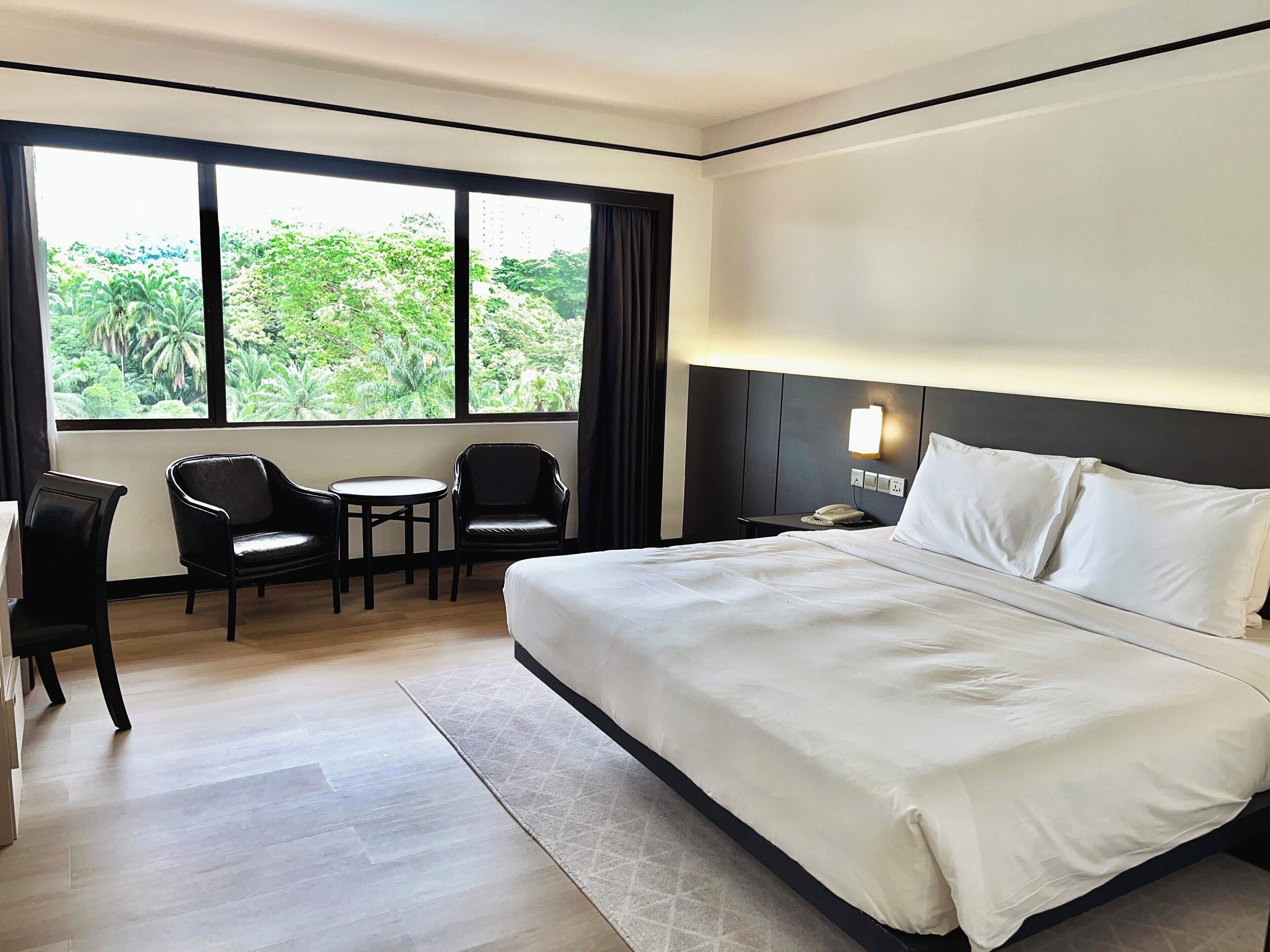 Una habitación de hotel con una cama grande, dos sillas, una mesita pequeña y una mesita de noche con un teléfono.