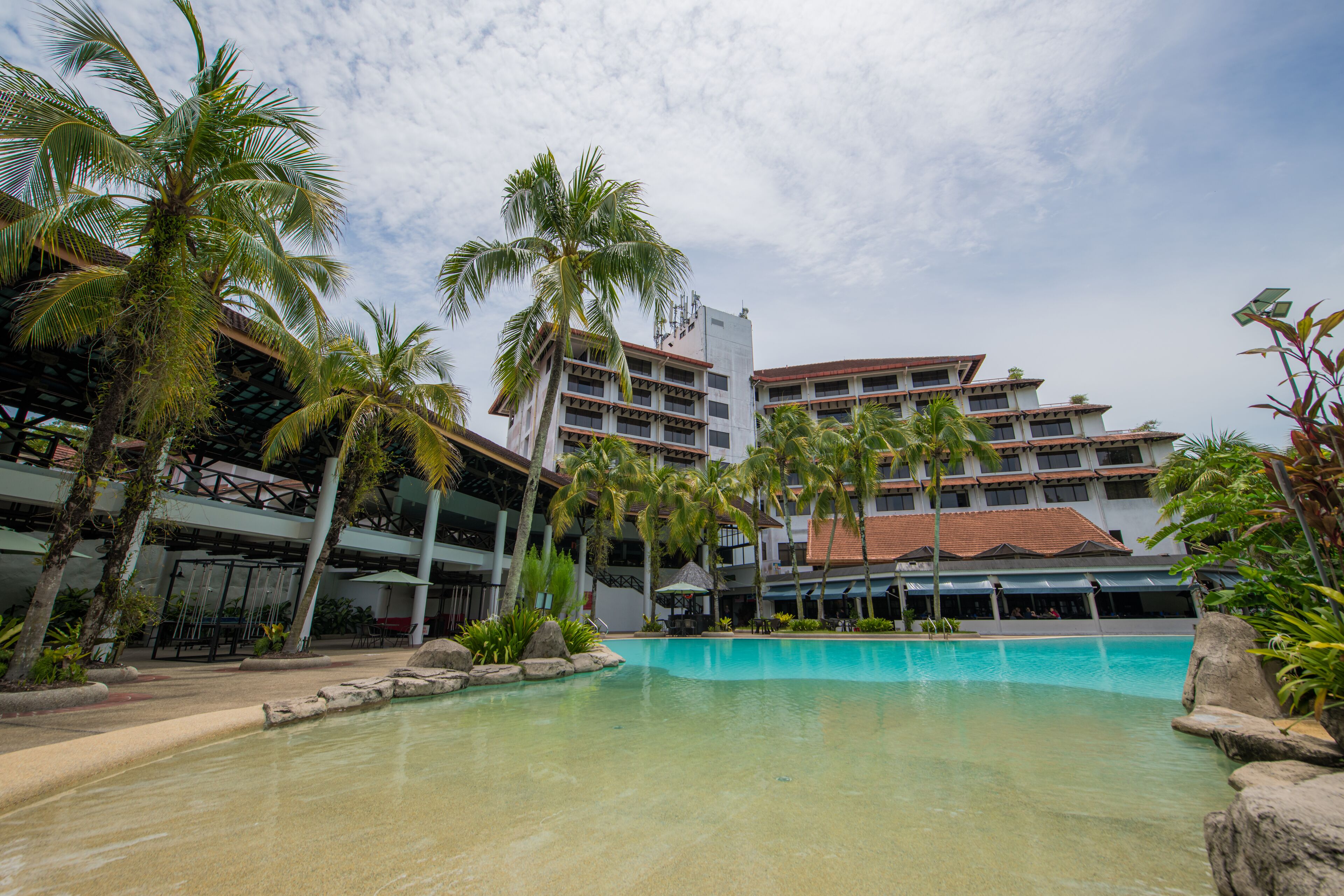 A hotel with a swimming pool surrounded by palm trees and a multi-story building with balconies.