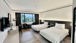 Ein Hotelzimmer mit zwei Betten, einem Schreibtisch, einem Stuhl, einem Fernseher und einem Fenster mit Blick auf Grünflächen.