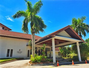 A hotel with a covered entrance, palm trees, and a clear blue sky. - Sabah Hotel Sandakan (Sandakan)