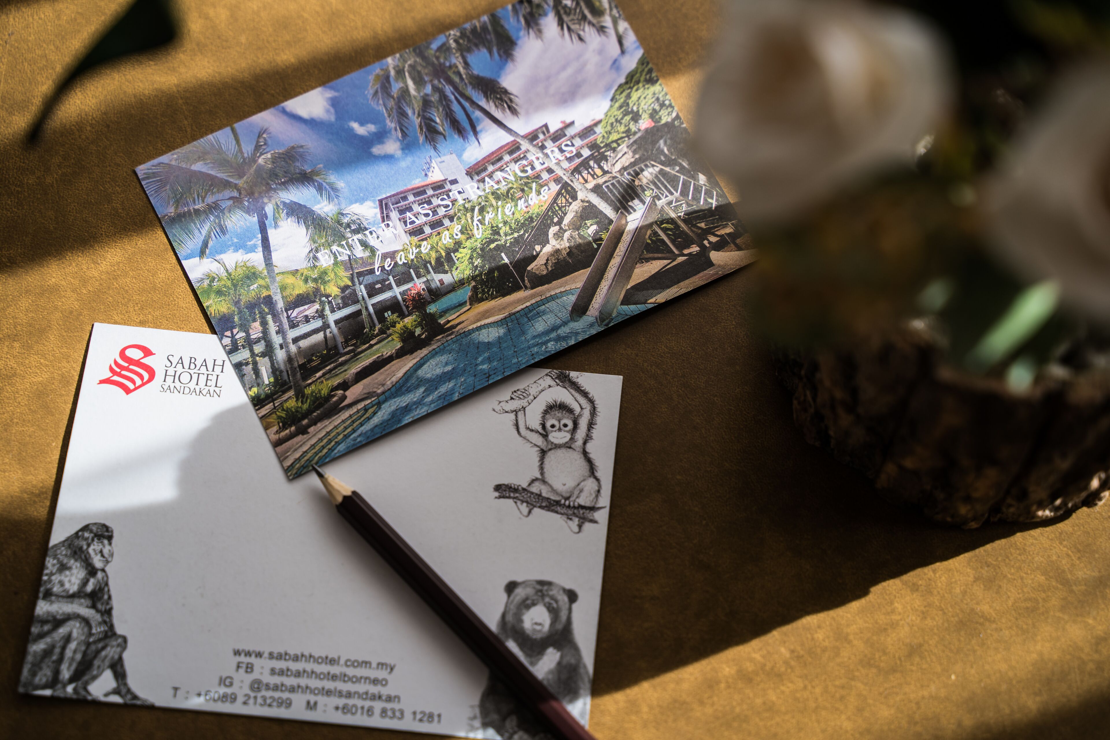 A business card and a brochure for Sabah Hotel Sandakan, featuring a resort with a pool and palm trees.