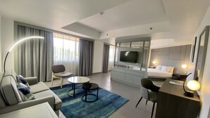 Ein modernes Hotelzimmer mit Wohnbereich, Esstisch, Sofa, Fernseher und Bett.