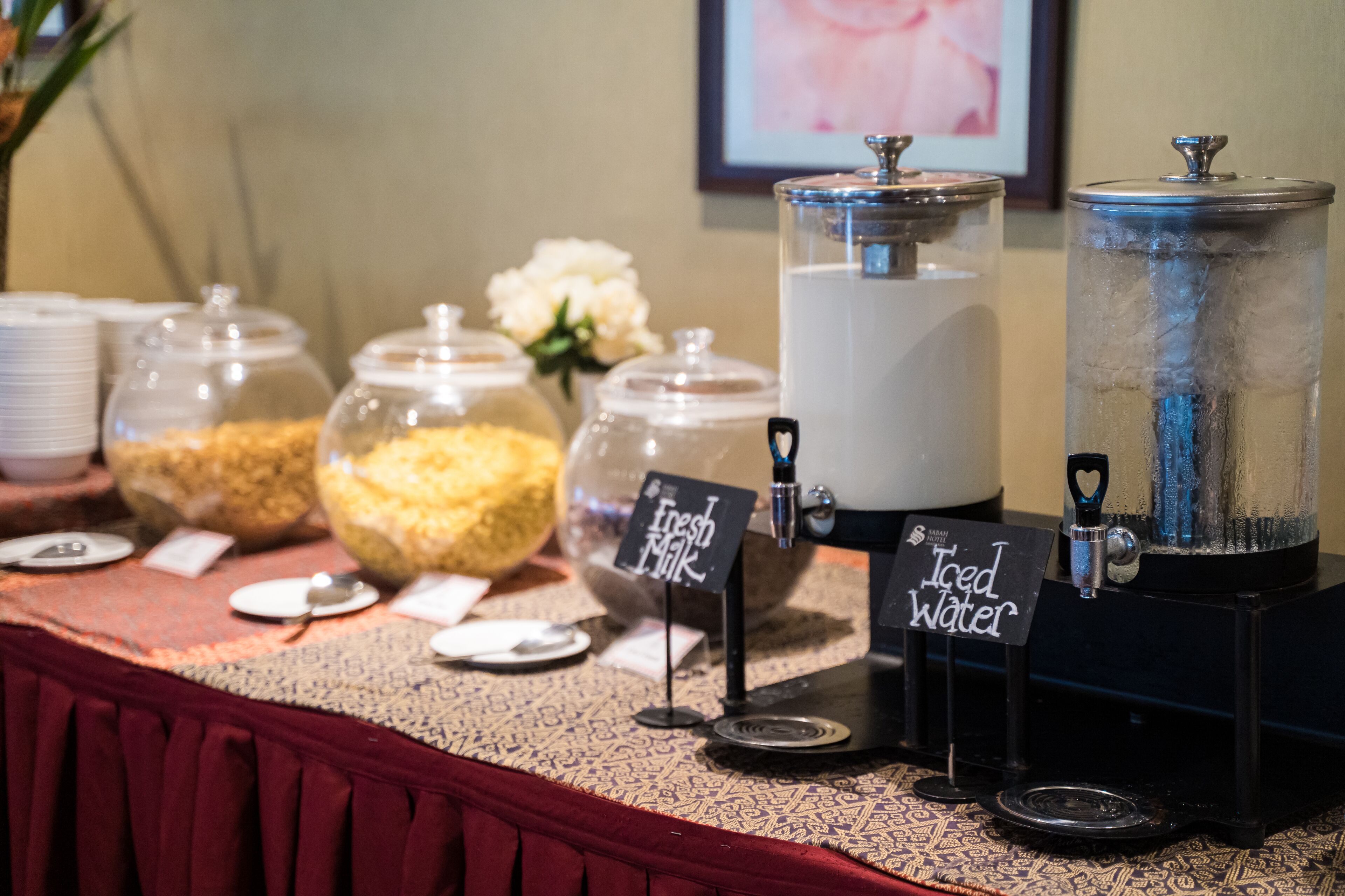 Disposición de bufé con varios recipientes de comida, un cartel que indica agua helada y una máquina de café.