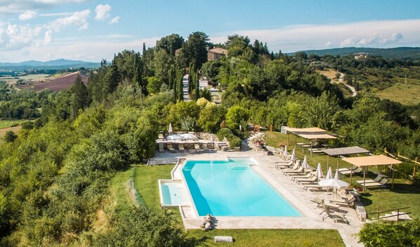 An aerial view of a resort with a swimming pool, lounge chairs, and a stone pathway leading to a stone structure. - Laticastelli Country Relais (Rapolano Terme)