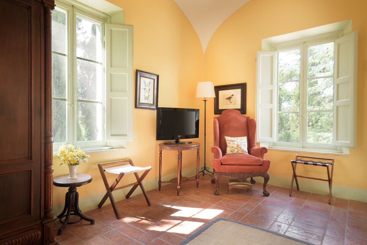 A room with a wooden chair, a small table with a vase, a television, and a lamp.