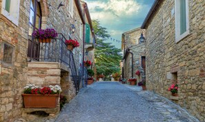 A narrow cobblestone street flanked by stone buildings with flower boxes and hanging lights. - Laticastelli Country Relais (Rapolano Terme)
