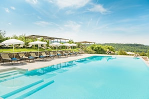 A swimming pool with lounge chairs and umbrellas, surrounded by greenery and a clear sky. - Laticastelli Country Relais (Rapolano Terme)