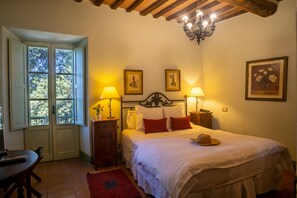 A bedroom with a bed, two bedside lamps, a wooden nightstand, a door with a view, and a chandelier. - Laticastelli Country Relais (Rapolano Terme)