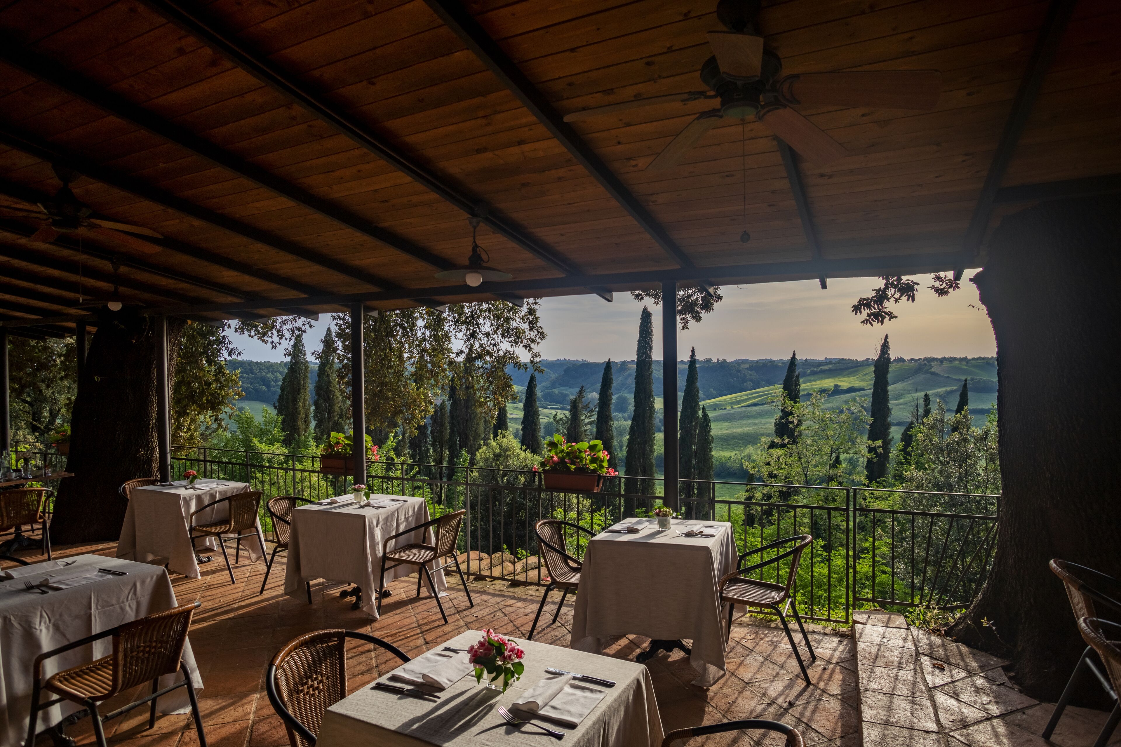 An outdoor terrace with tables and chairs, overlooking a scenic landscape with trees and hills.