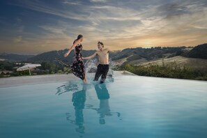 A couple playing in a swimming pool with a scenic view of hills and a sunset in the background. - Laticastelli Country Relais (Rapolano Terme)