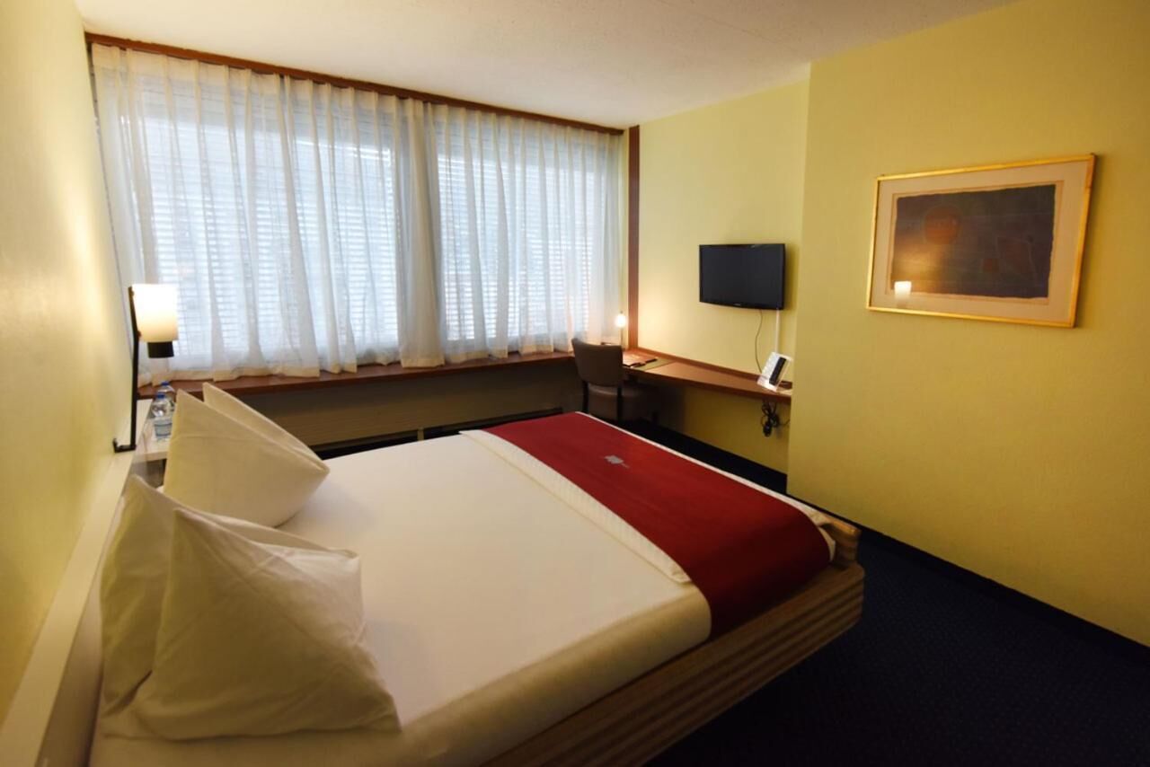 A hotel room with a bed, a desk, a chair, a television, and a framed picture on the wall.