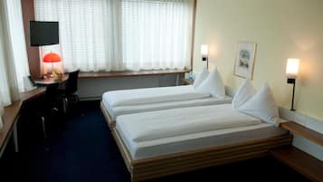 A hotel room with two beds, a desk with a computer and lamp, and a window with curtains.