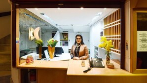 Un comptoir d’accueil avec une personne derrière, un téléphone, une petite boîte étiquetée « CAPITALS CLUB » et un vase rempli de fleurs jaunes.