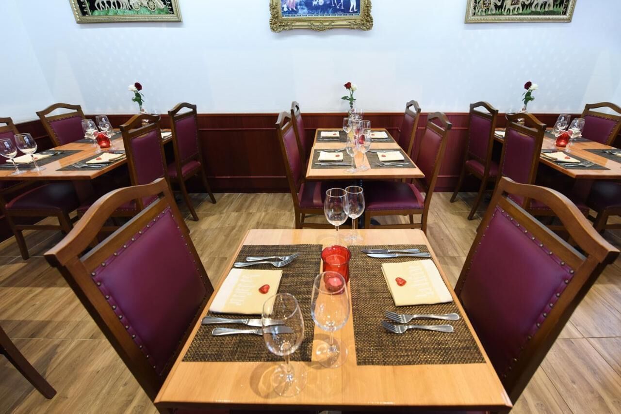 A restaurant with wooden tables and purple upholstered chairs. Each table is set with wine glasses, cutlery, and a red candle.