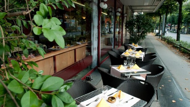 Un restaurant en plein air avec des tables, des chaises, un comptoir et de la verdure.