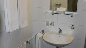 Un baño con un lavamanos blanco, un espejo y un estante de vidrio sobre el lavamanos.