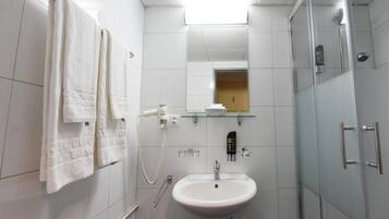 A modern bathroom with a white sink, glass shower enclosure, and towels hanging on the wall.