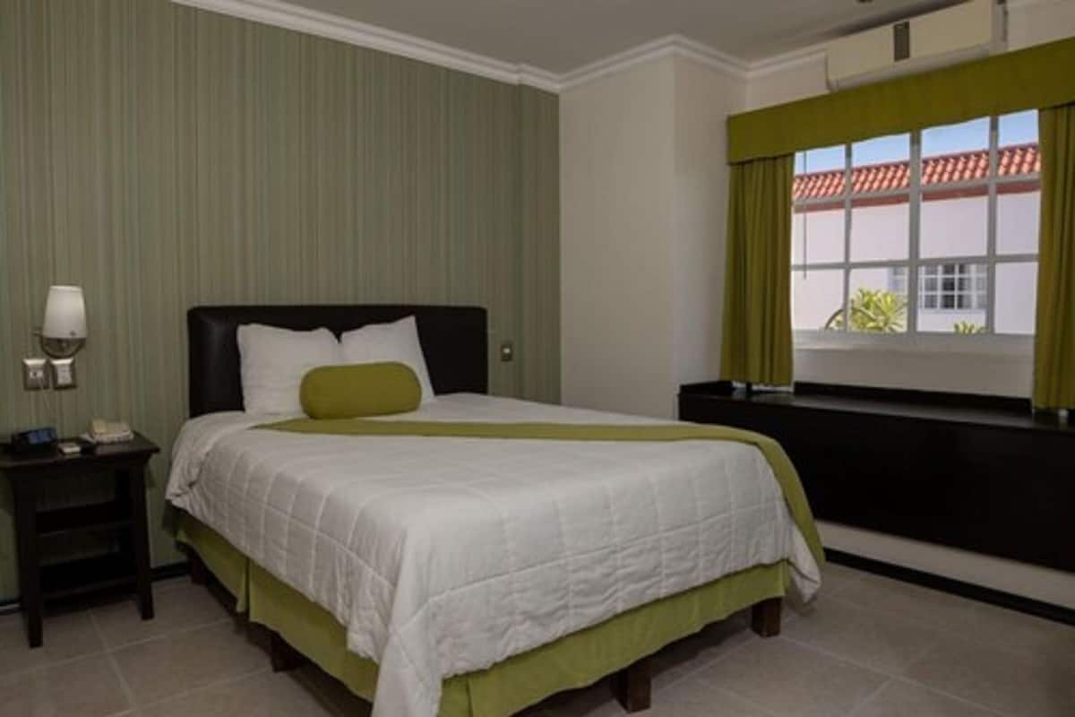 Una camera d'albergo con un letto, un comodino, una finestra con tende e vista sull'esterno.