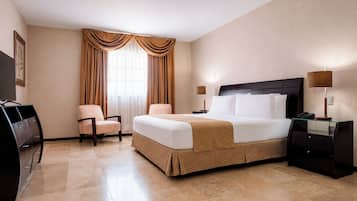 Una habitación de hotel con una cama, dos sillas, un escritorio, un televisor y una lámpara.
