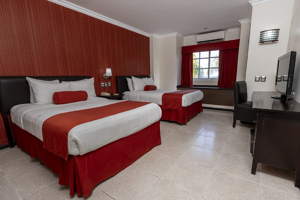 Una camera d'albergo con due letti, una scrivania, una TV e una finestra con tende rosse.