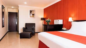 Habitació d'hotel amb llit, una cadira, una taula de nit, una làmpada i un televisor fixat a la paret.