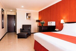 Una camera d'albergo con un letto, una sedia, un comodino, una lampada e una TV a parete.