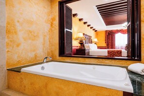 Un bagno con una vasca, uno specchio che riflette una camera da letto e una finestra con persiane.