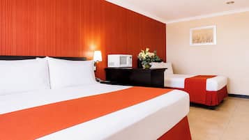 A hotel room with a large bed, a bedside table with a lamp, a microwave, and a small table with flowers.